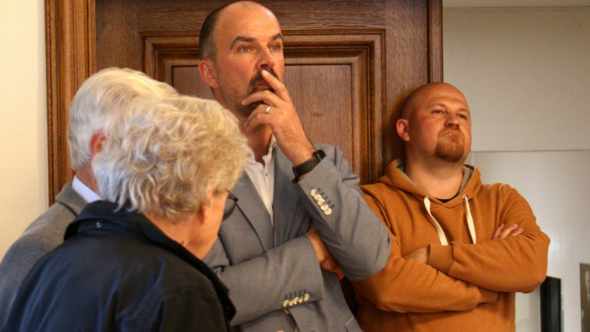 Martin Finder lehnt mit missmutigem Gesichtsausdruck an der Tür des Ratsaals. Guido Waters hat die Hand vor dem Mund.