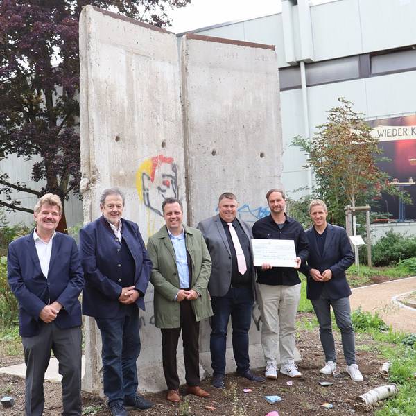 Politiker und der Schuldirektor der Marienschule Euskirchen Michael Mombaur stehen vor Originalelementen der Berliner Mauer.