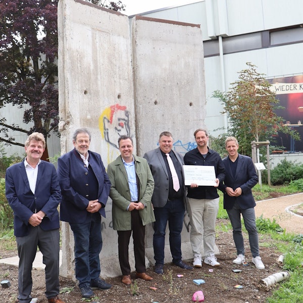 Politiker und der Schuldirektor der Marienschule Euskirchen Michael Mombaur stehen vor Originalelementen der Berliner Mauer.