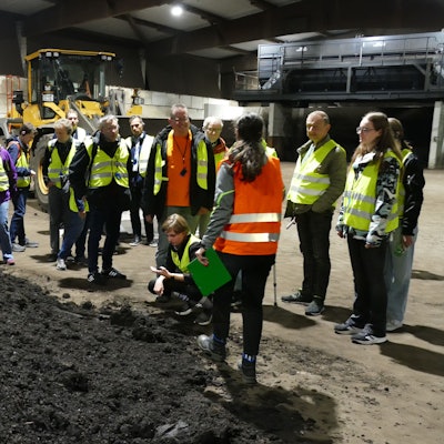 Männer und Frauen in Warnwesten stehen neben einem Erdhaufen.