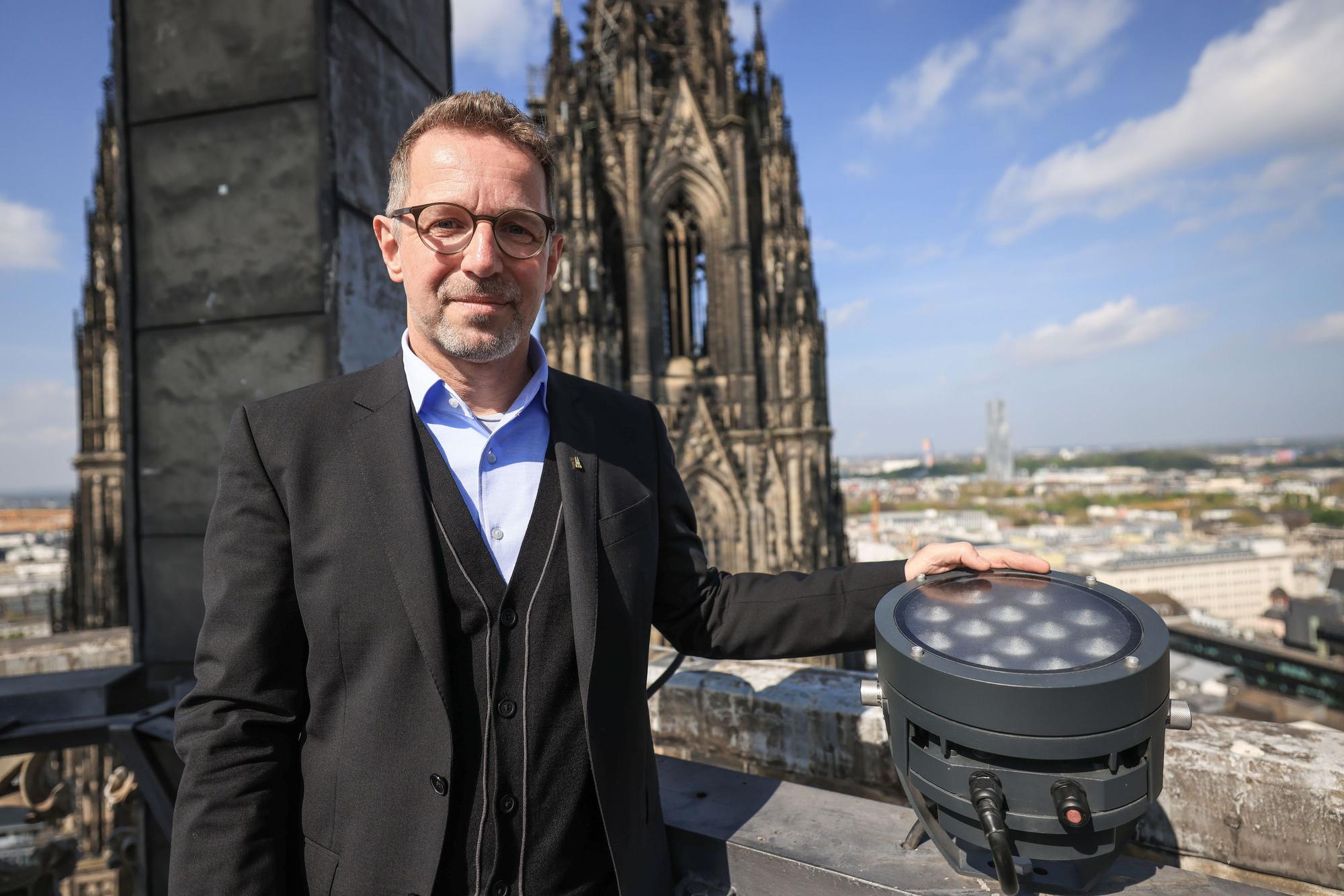 PRODUKTION - 14.04.2025, Nordrhein-Westfalen, Köln: Peter Füssenich, Dombaumeister, steht im Vierungsturm neben einer neuen LED-Lampe. Der Kölner Dom wird von Ostersonntag an komplett neu angestrahlt. (zu dpa: «Kölner Dom ab Ostern mit neuer Beleuchtung») Foto: Oliver Berg/dpa +++ dpa-Bildfunk +++