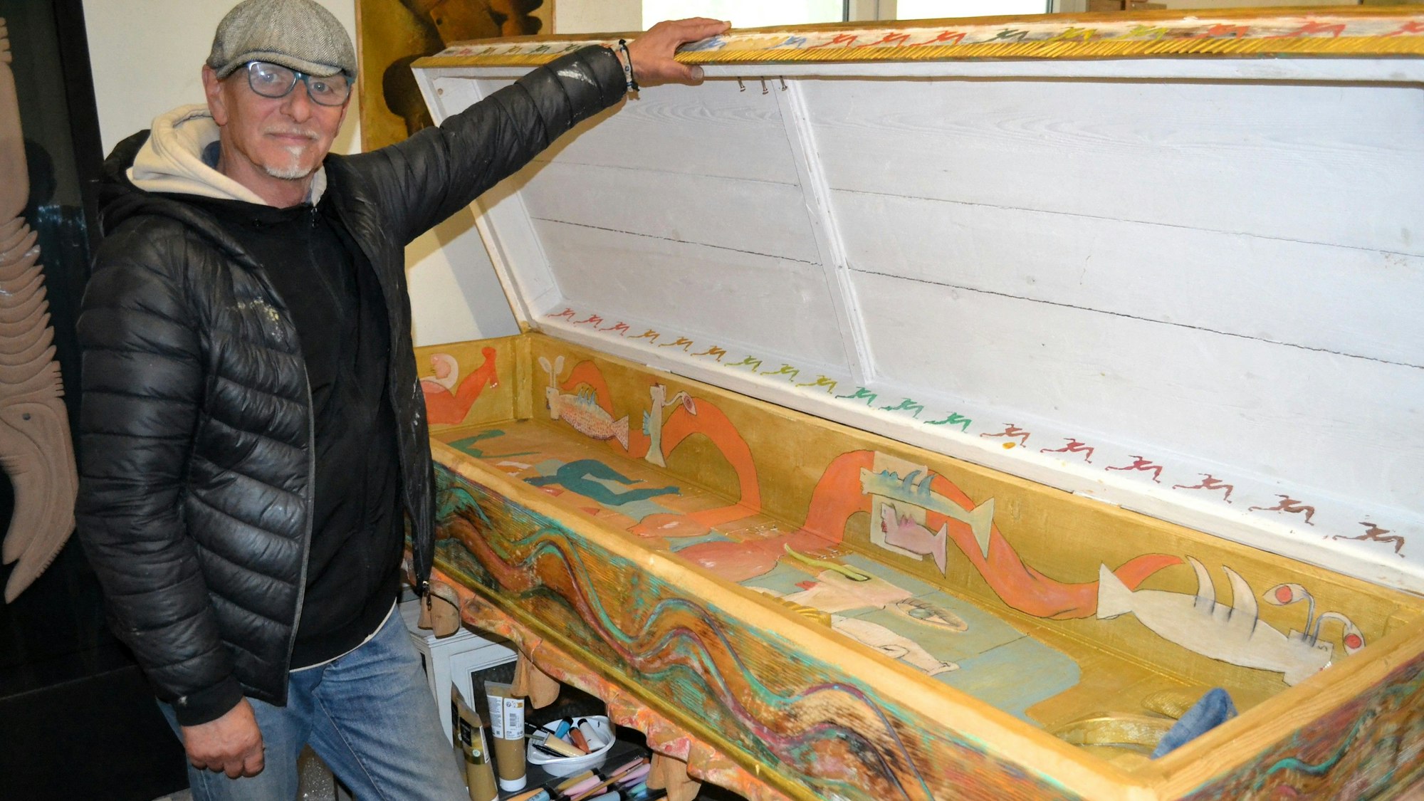 Ein Mann steht neben einem offenen, bunt bemalten Sarg.