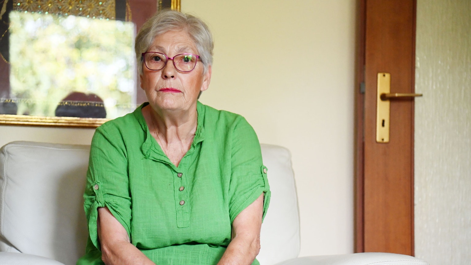 Eine ältere Frau trägt Brille und sitzt auf einem Sessel.