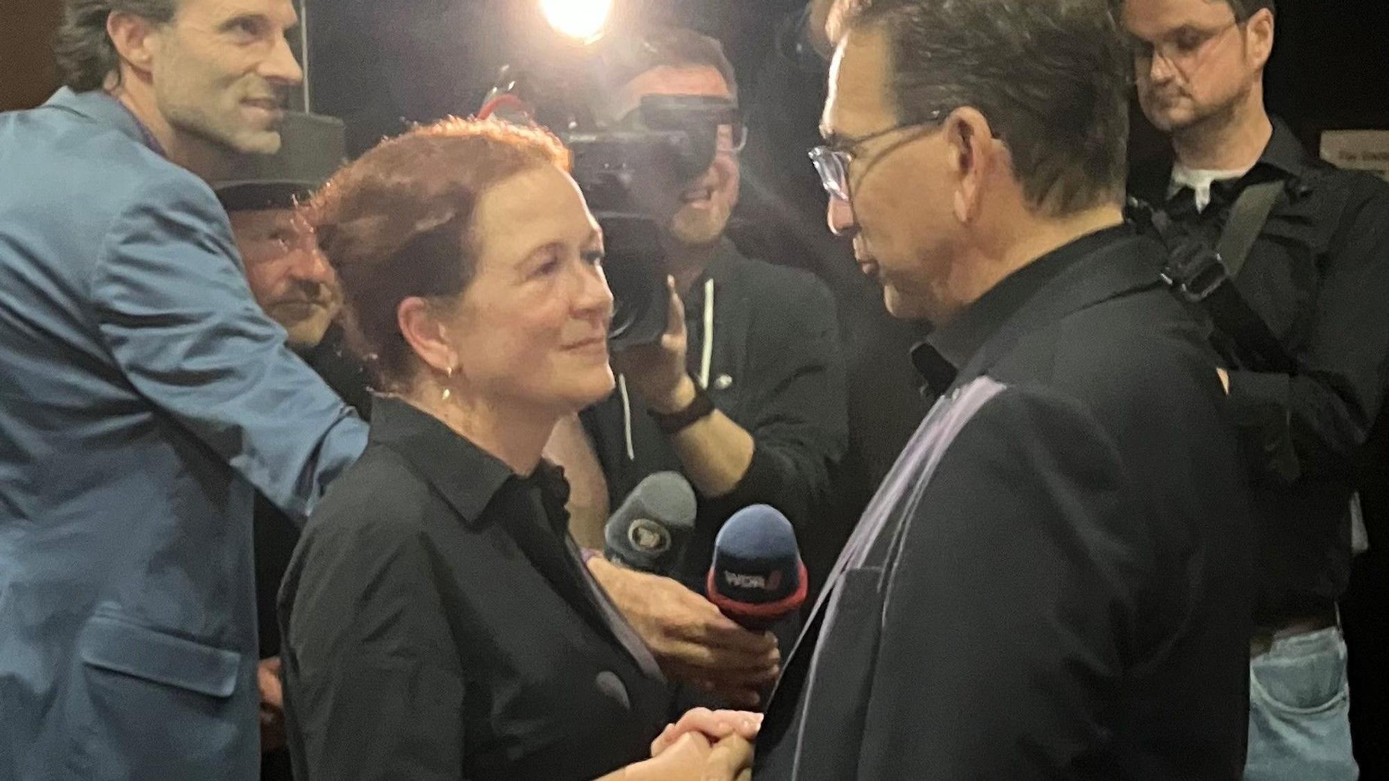 Ein Mann und eine Frau geben sich die Hand. Ein Mann mit Kamera filmt die Szene.