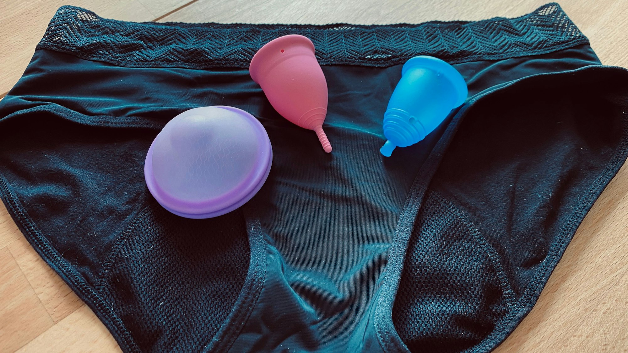 Periodentassen und eine Periodenscheibe liegen auf einer Menstruationsunterhose.