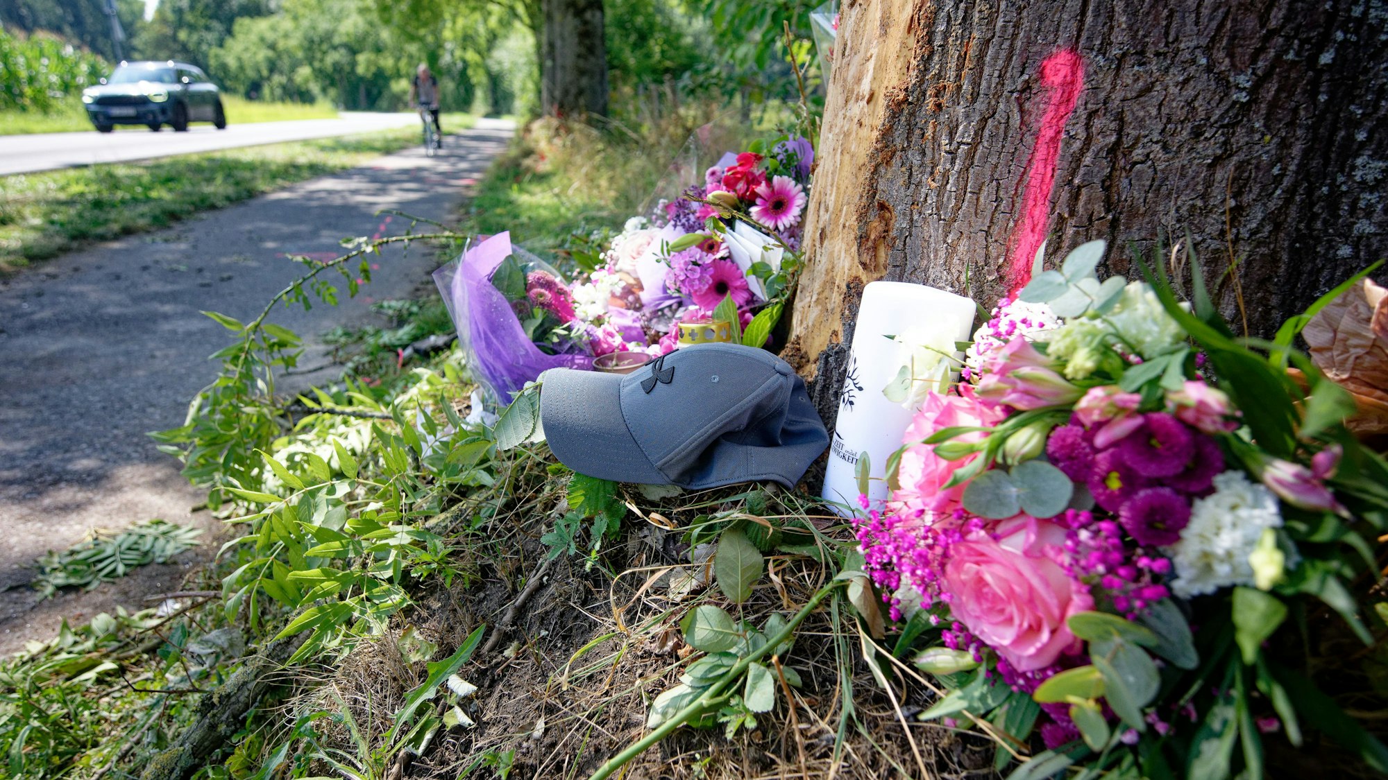 Blumen, Kerzen und eine Mütze liegen an einer Unfallstelle bei Monheim am Rhein.