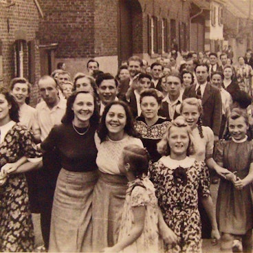 Zu sehen sind viele Menschen auf einer Dorfstraße auf einem Schwarz-Weiß-Foto.