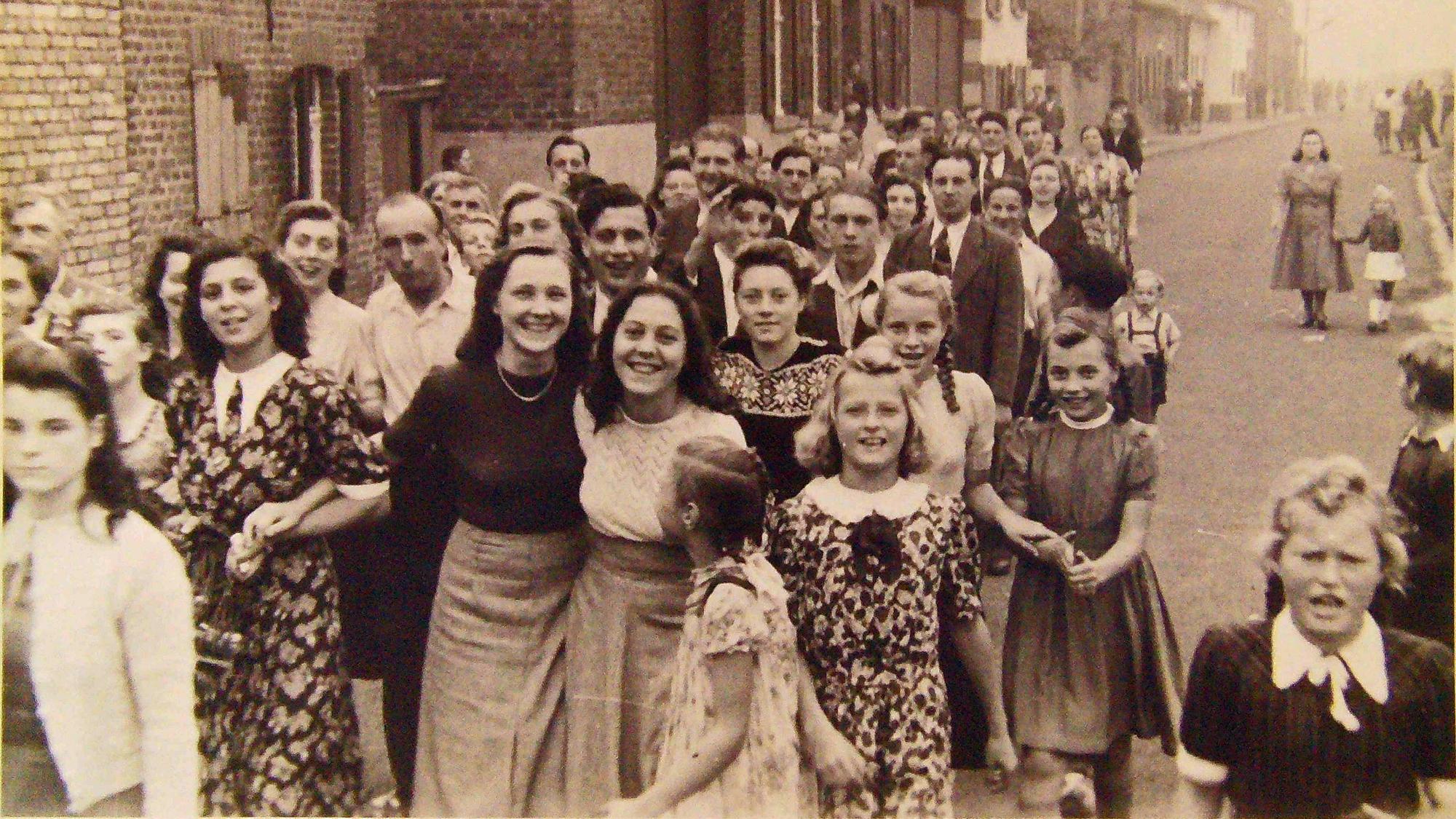 Zu sehen sind viele Menschen auf einer Dorfstraße auf einem Schwarz-Weiß-Foto.