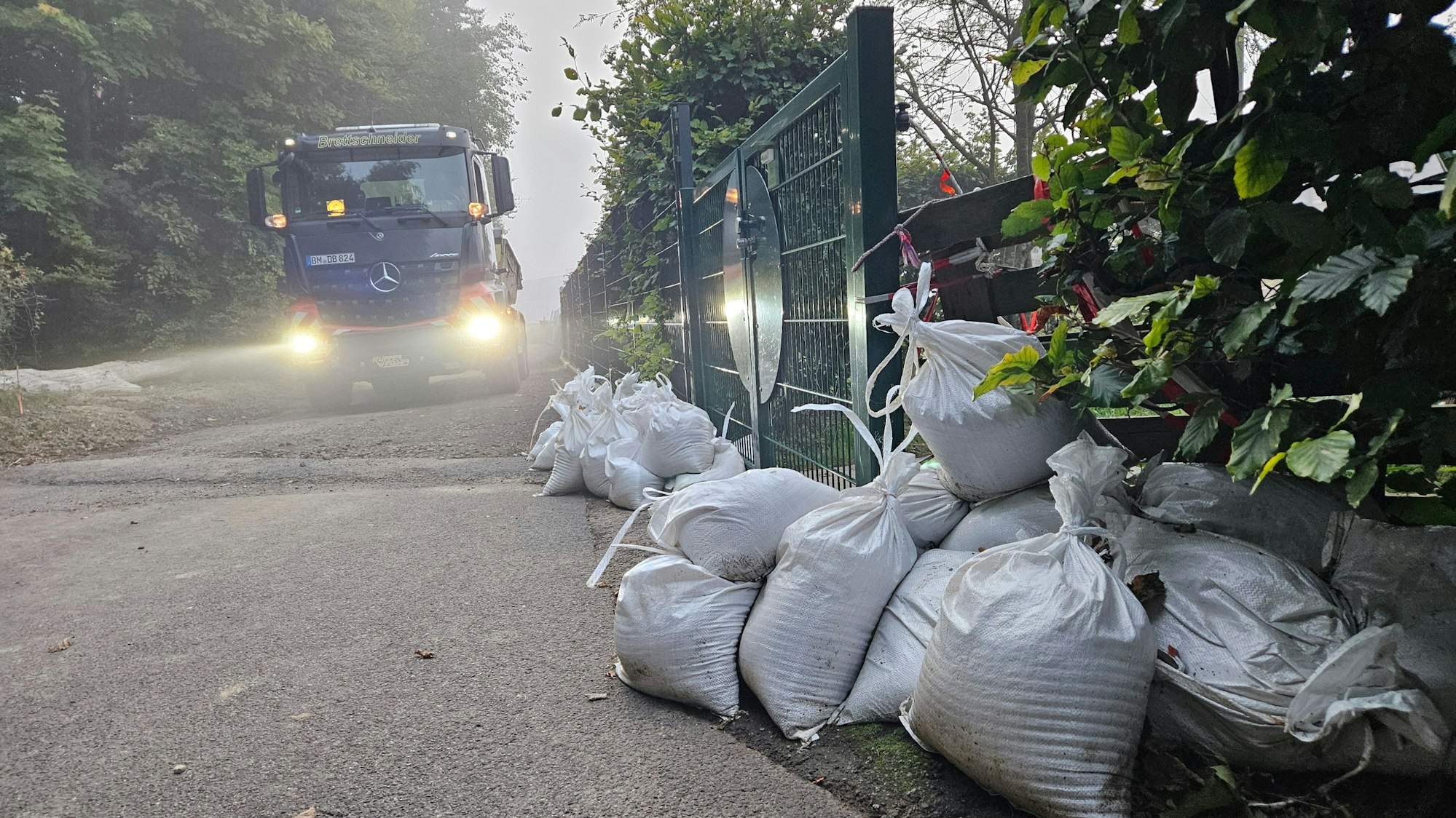 Zu sehen sind Sandsäcke vor einem Zaun, auf einem Weg daneben fährt ein Lastwagen.