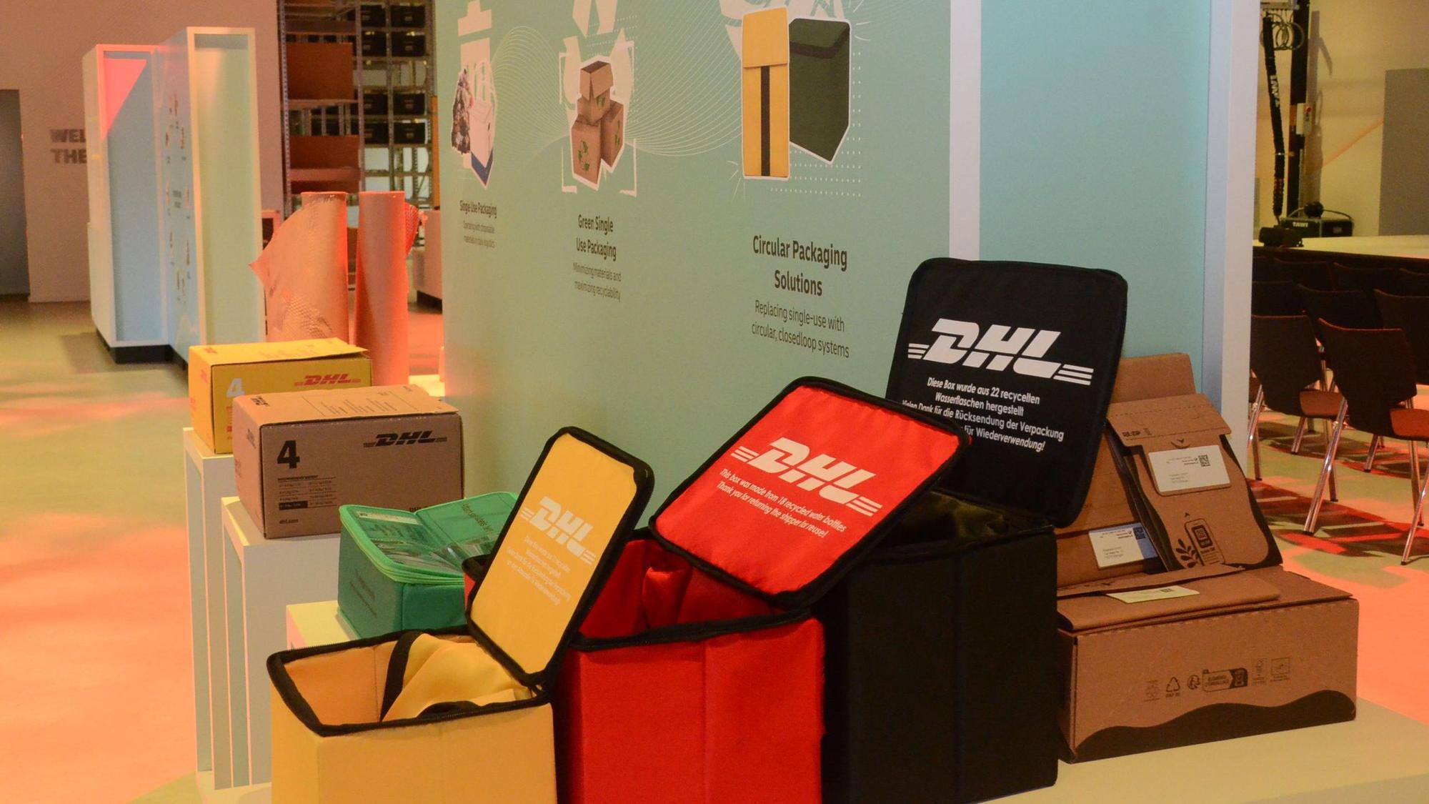 Boxen mit dem Aufdruck DHL in Rot, Grün, Gelb und Schwarz.