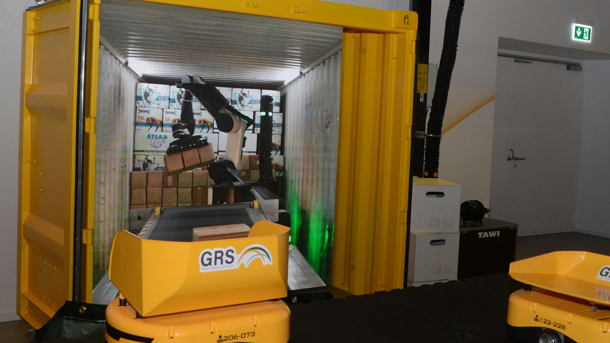 Ein gelber Container, im Hintergrund zeigt ein Film das Entladen durch einen Roboterarm.