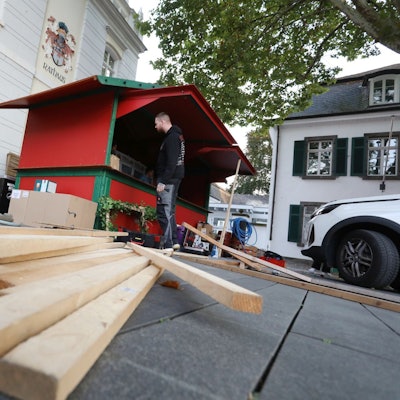 Holzlatten liegen vor einer rot-grünen Bude, die gerade aufgebaut wird.