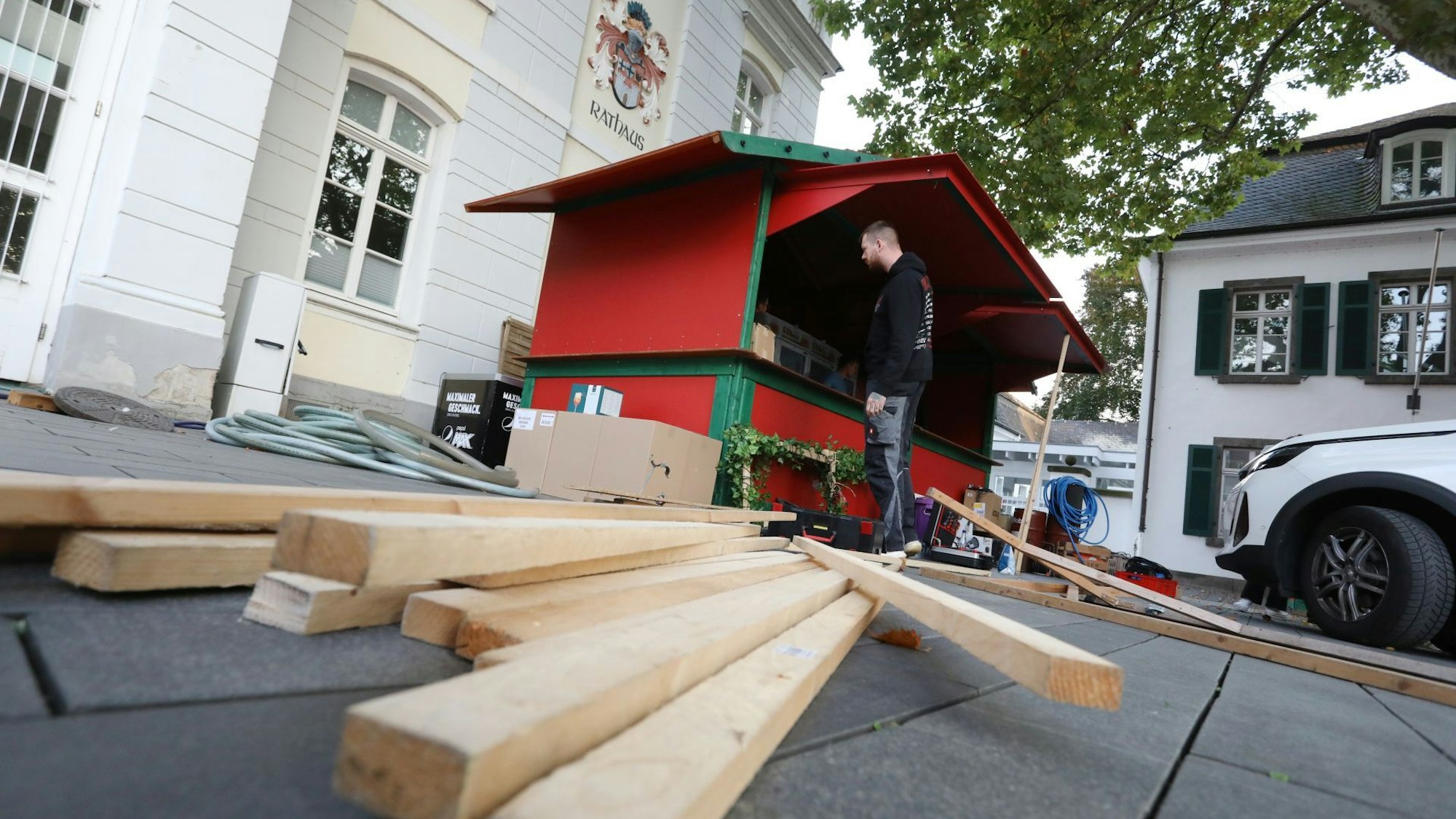 Holzlatten liegen vor einer rot-grünen Bude, die gerade aufgebaut wird.