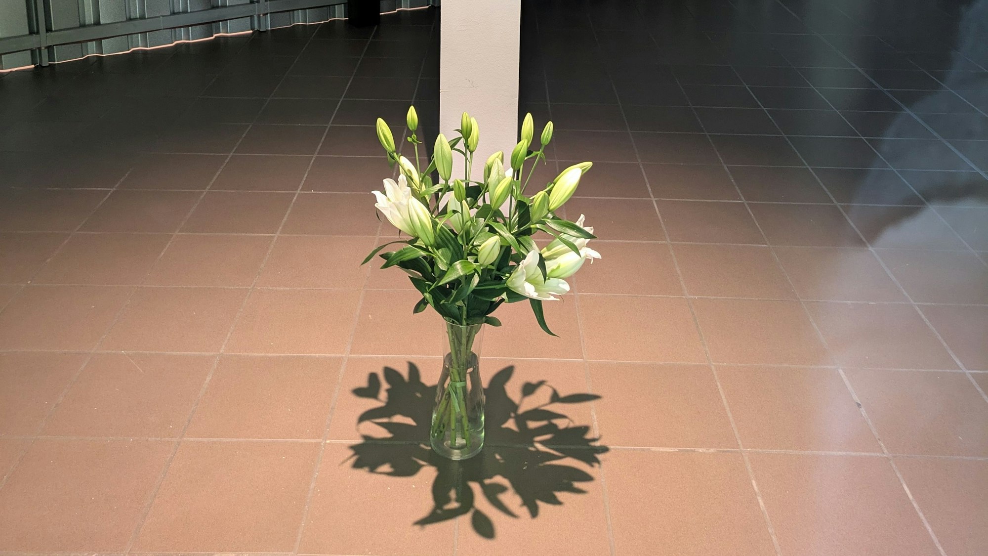 Ein Strauß weiße Lilien steht in einem leeren Raum auf dem Boden.