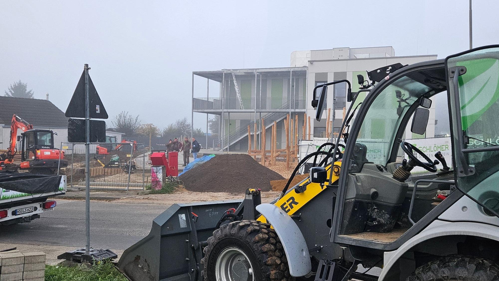 Zu sehen ist ein kleiner Bagger vor einer Baustelle.
