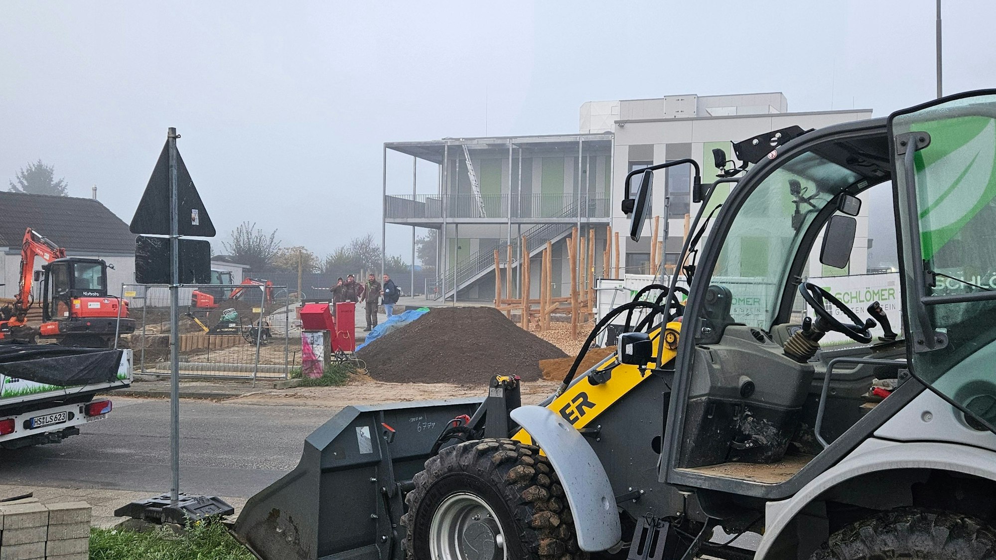 Zu sehen ist ein kleiner Bagger vor einer Baustelle.