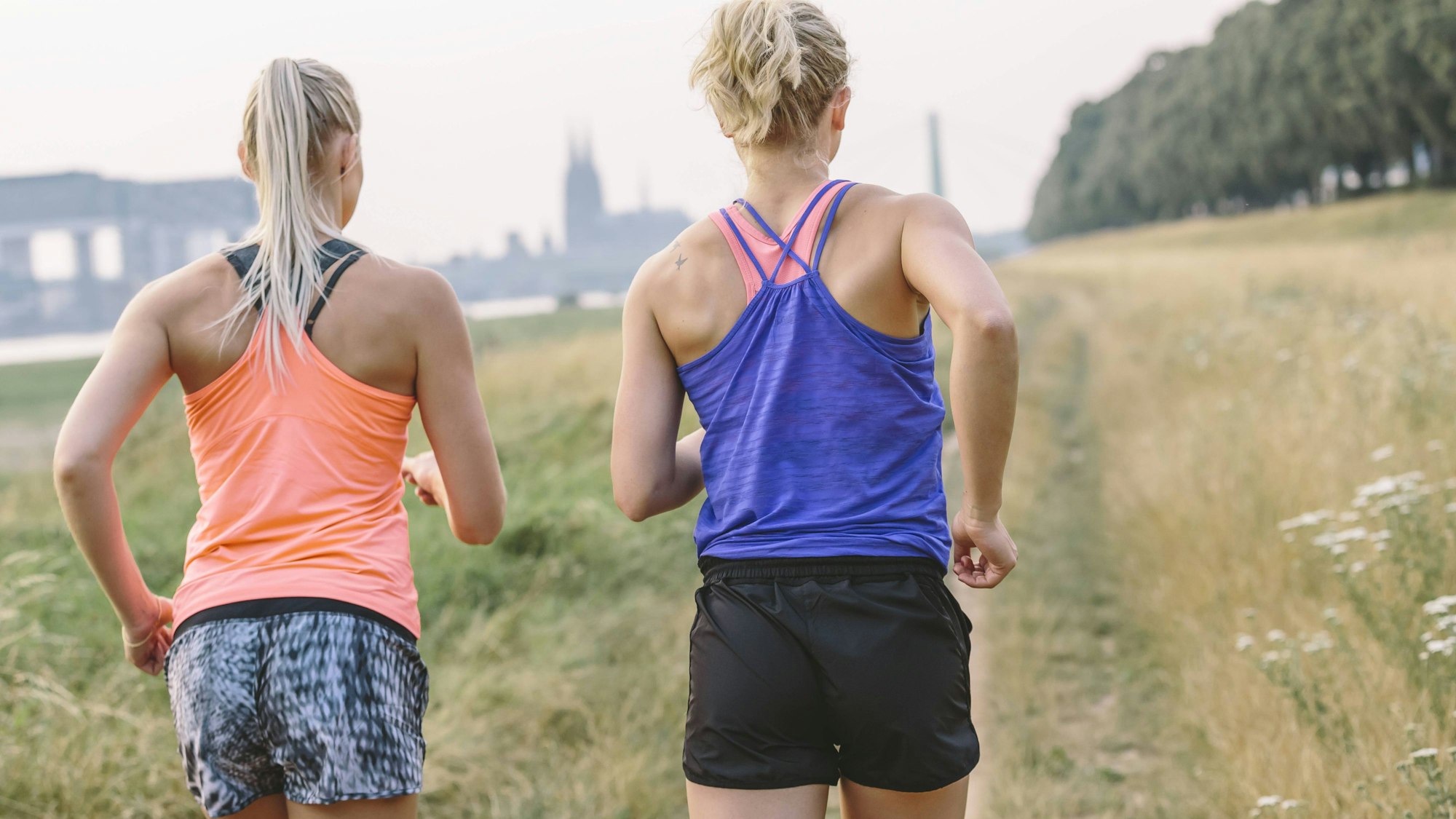 Zwei Frauen joggen am Rheinufer. Sie sind von hinten zu sehen.