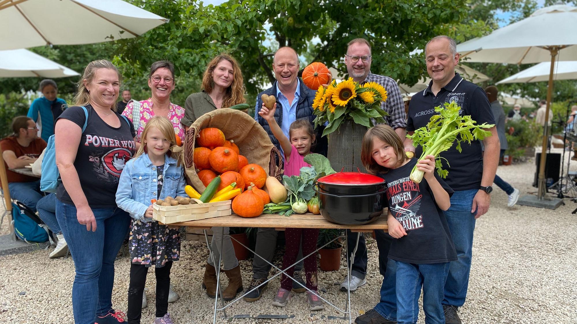 Das Foto zeigt eine Gruppe von Menschen hinter einem Tisch mit Kürbissen, Gemüse und Sonnenblumen auf dem Gertrudenhof.