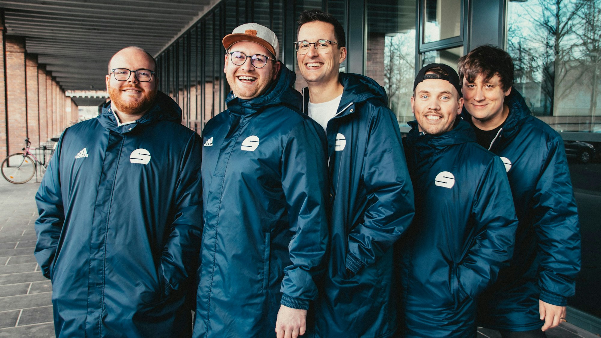 Fünf junge Männer in gleichen Windjacken.
