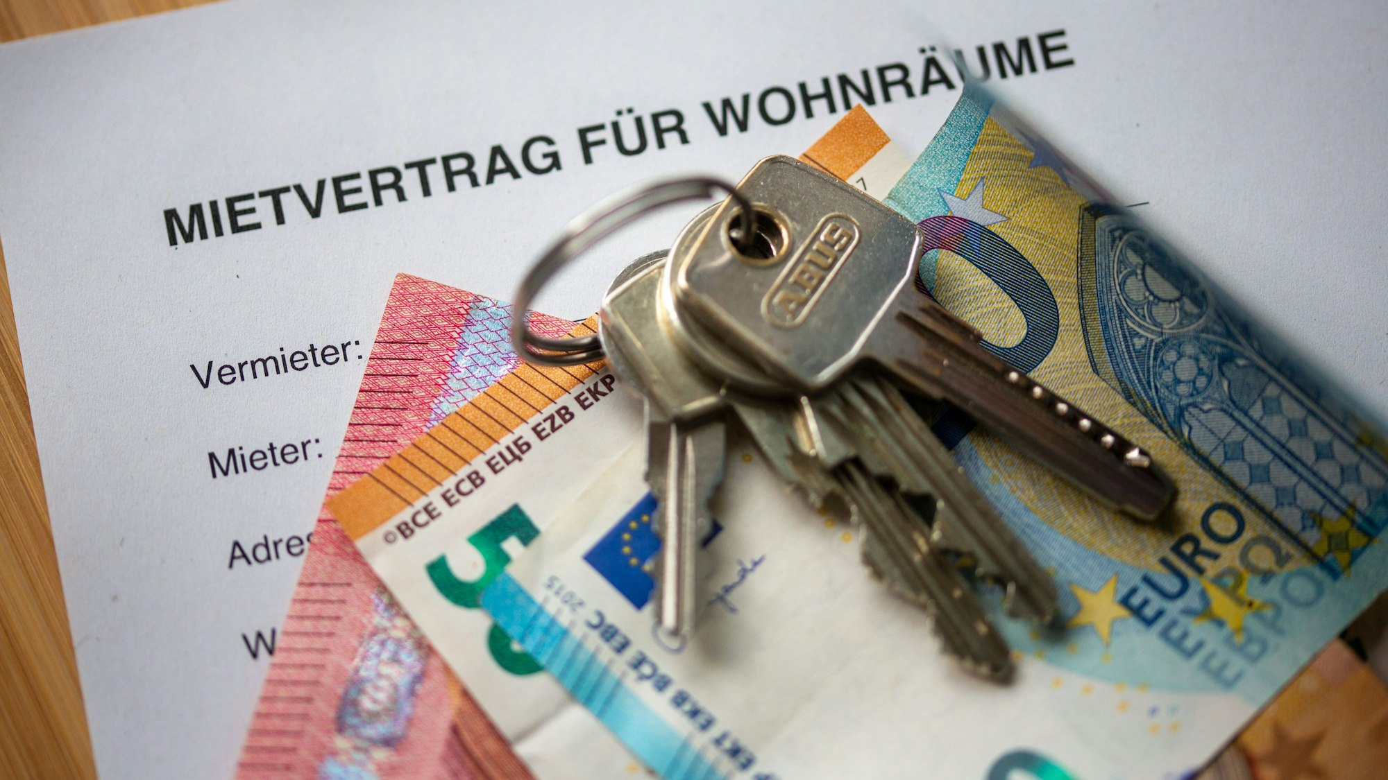 Ein Mietvertrag für Wohnräume liegt zusammen mit Geldscheinen und Wohnungsschlüsseln auf einem Tisch.