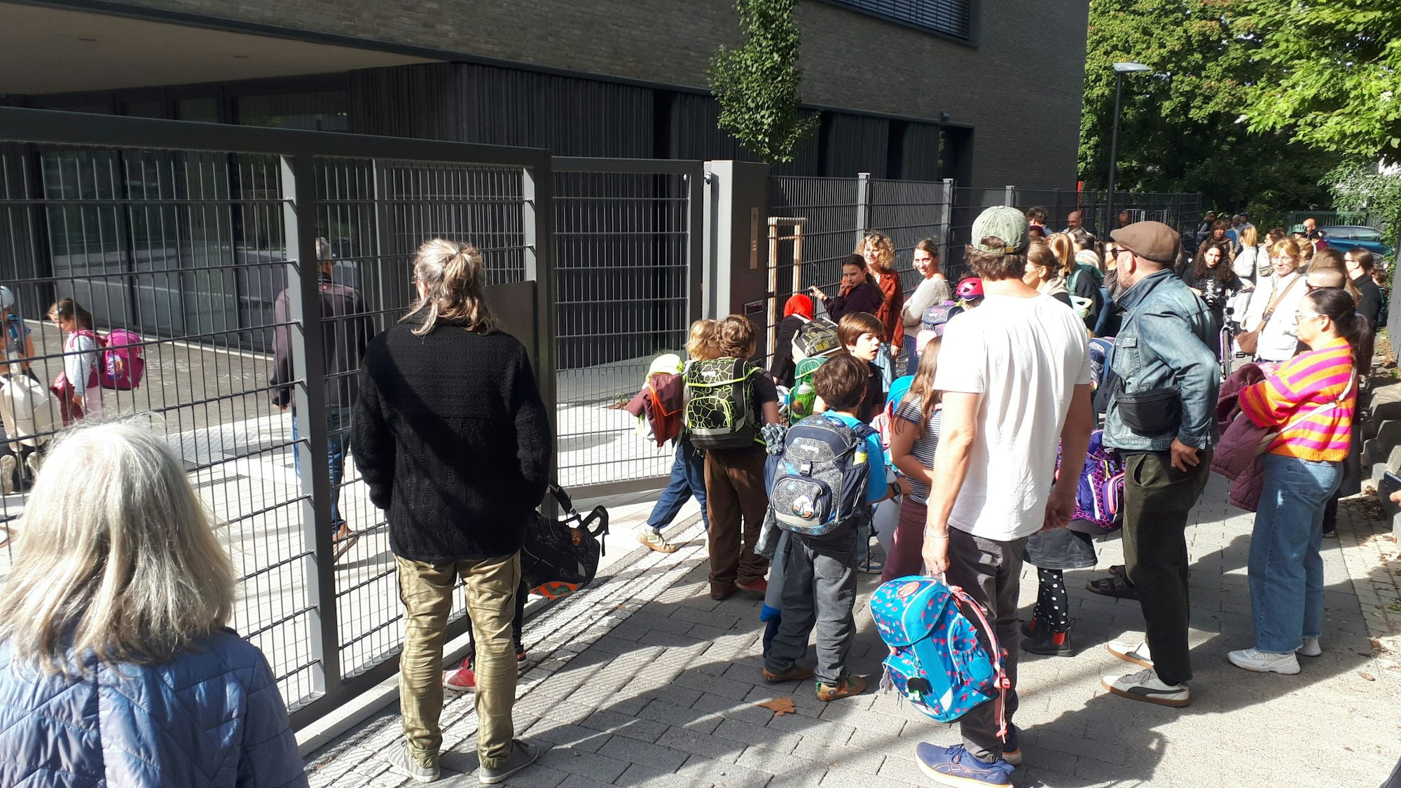 Viele Eltern stehen vor einem Gittertor.