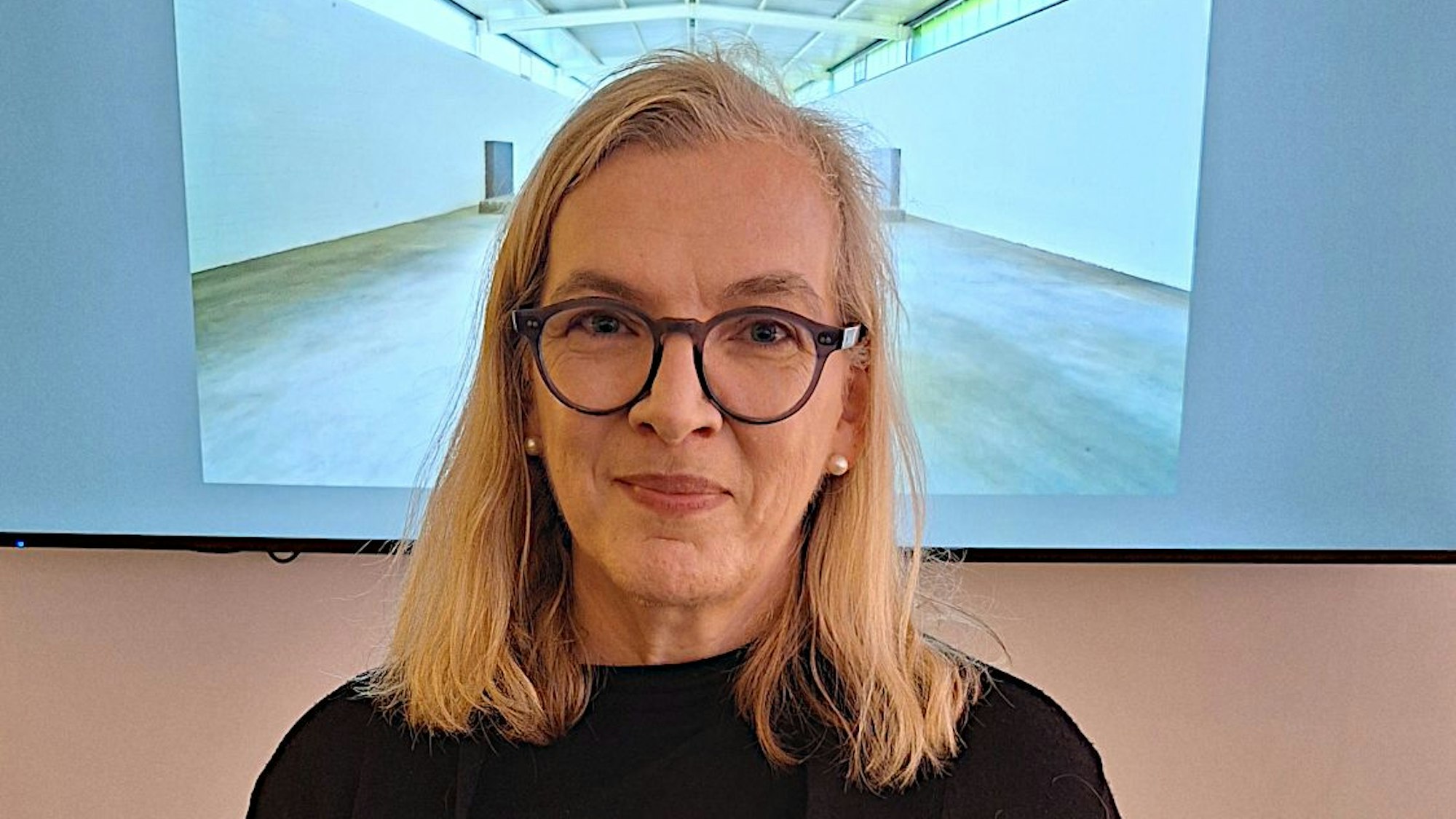 Juliane Rückriem steht vor einem Bild einer Halle, deren Mittelteil ihr Kopf verdeckt.