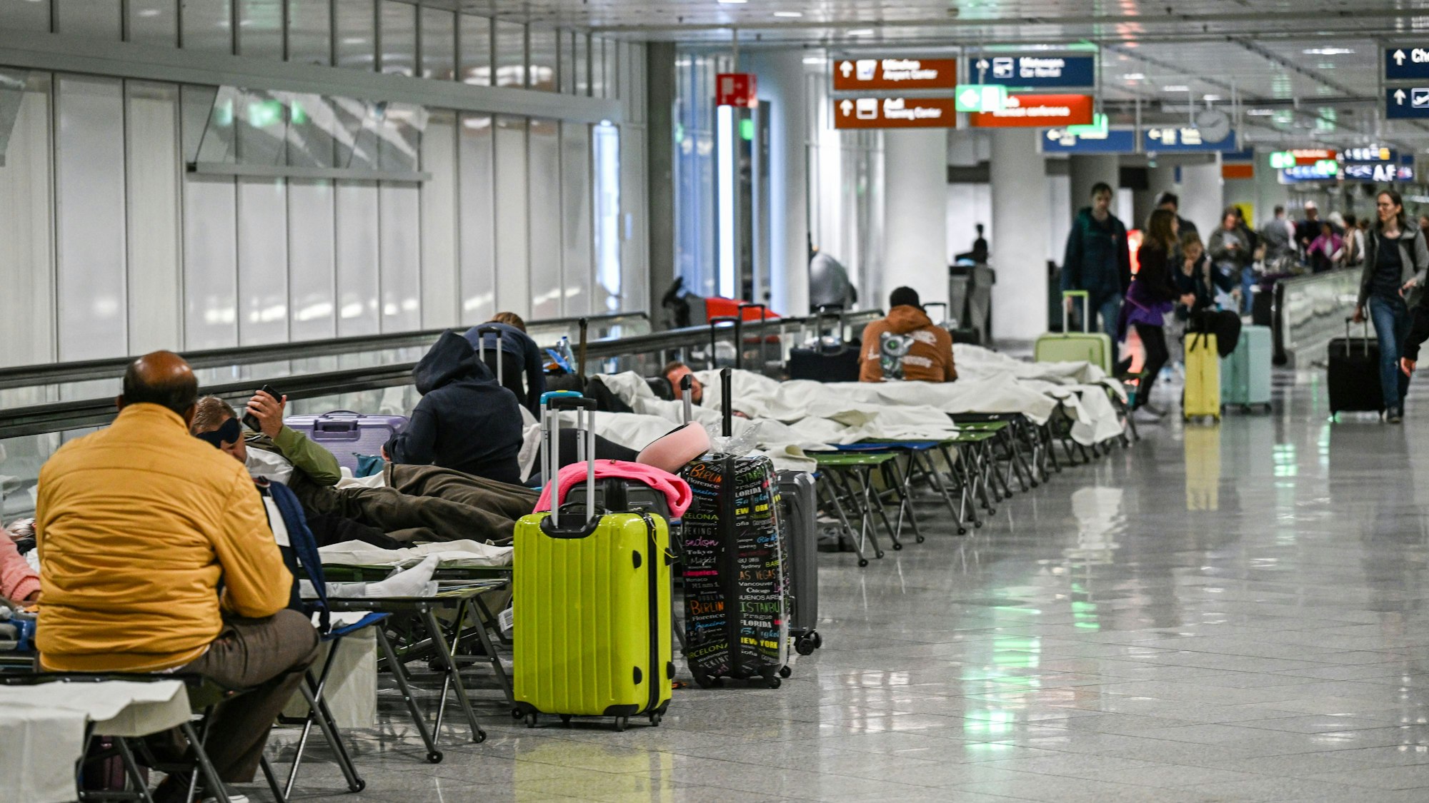 Menschen warten nach Drohnensichtungen und Flugausfällen in Flughafen München auf Feldbetten.