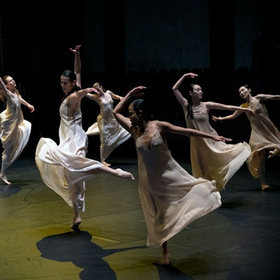 Tänzerinnen in weißen Kleiden springen und hüpfen elegant.