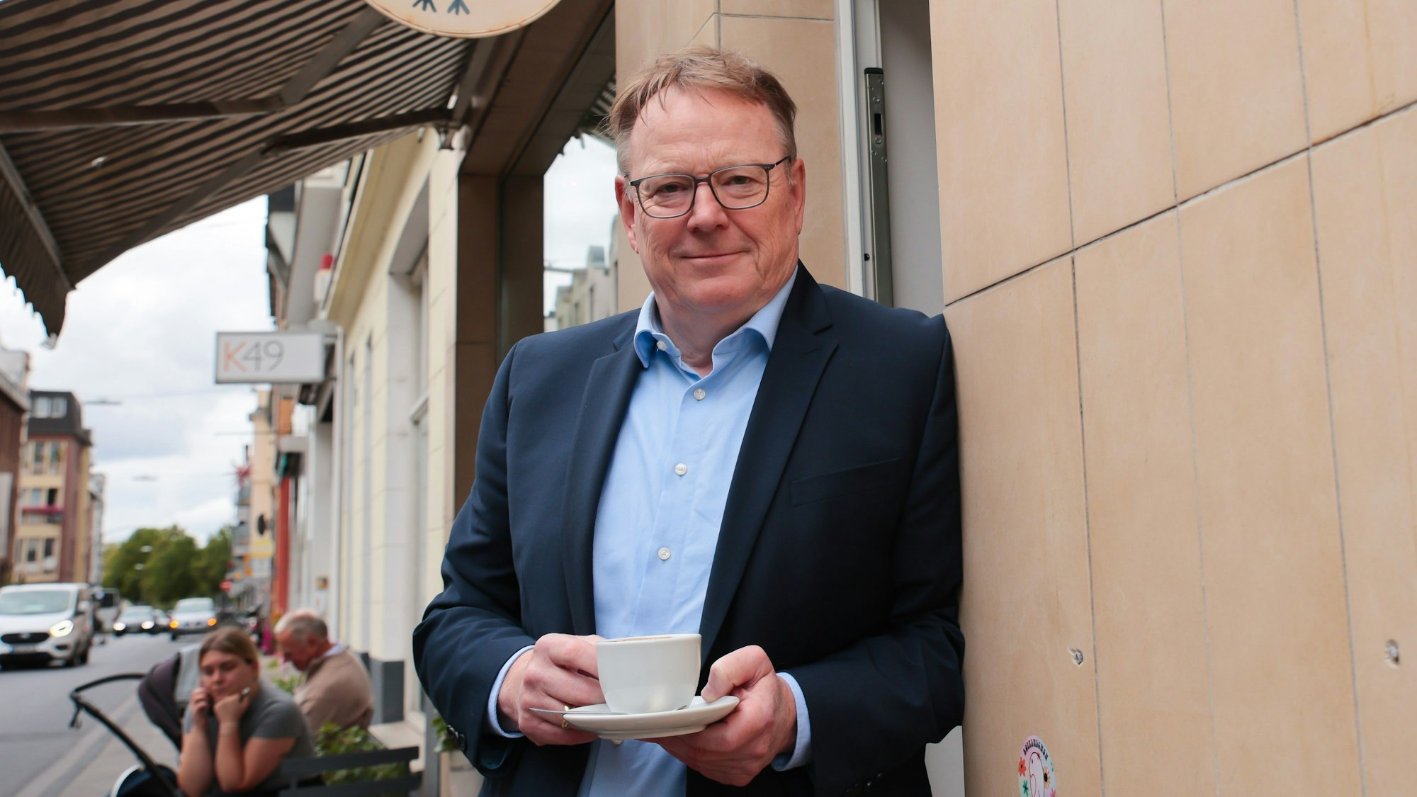 Torsten Burmester lehnt mit einer Kaffeetasse an einer Hauswand.