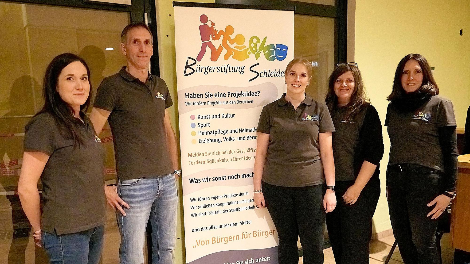 Ein Mann und vier Frauen stehen in identischen Poloshirts neben einem Roll-up-Display der Bürgerstiftung Schleiden.