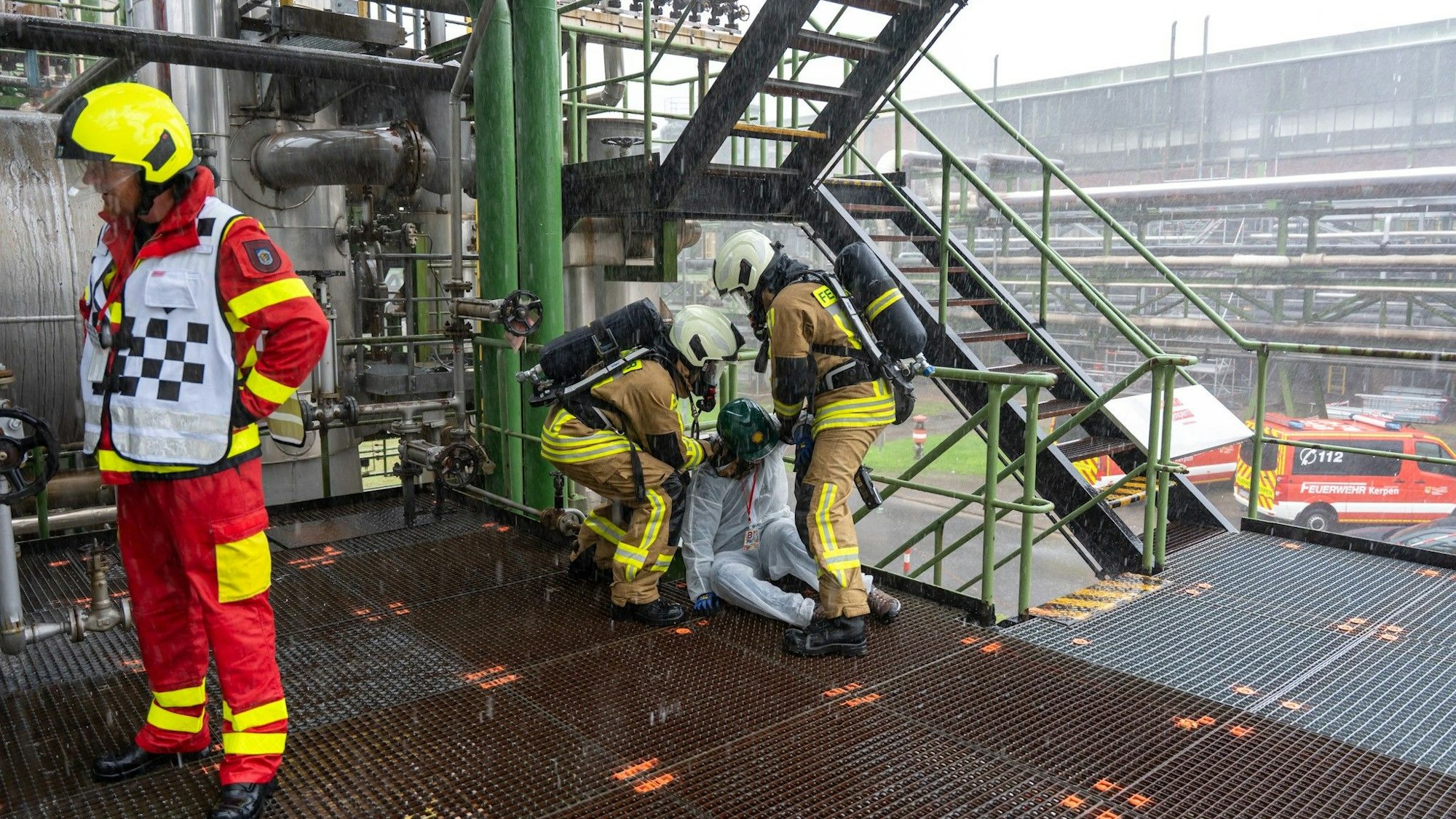 Zu sehen ist, wie Feuerwehrleute bei einer Übung einen Verletzten auf einem Fabrikgelände versorgen.