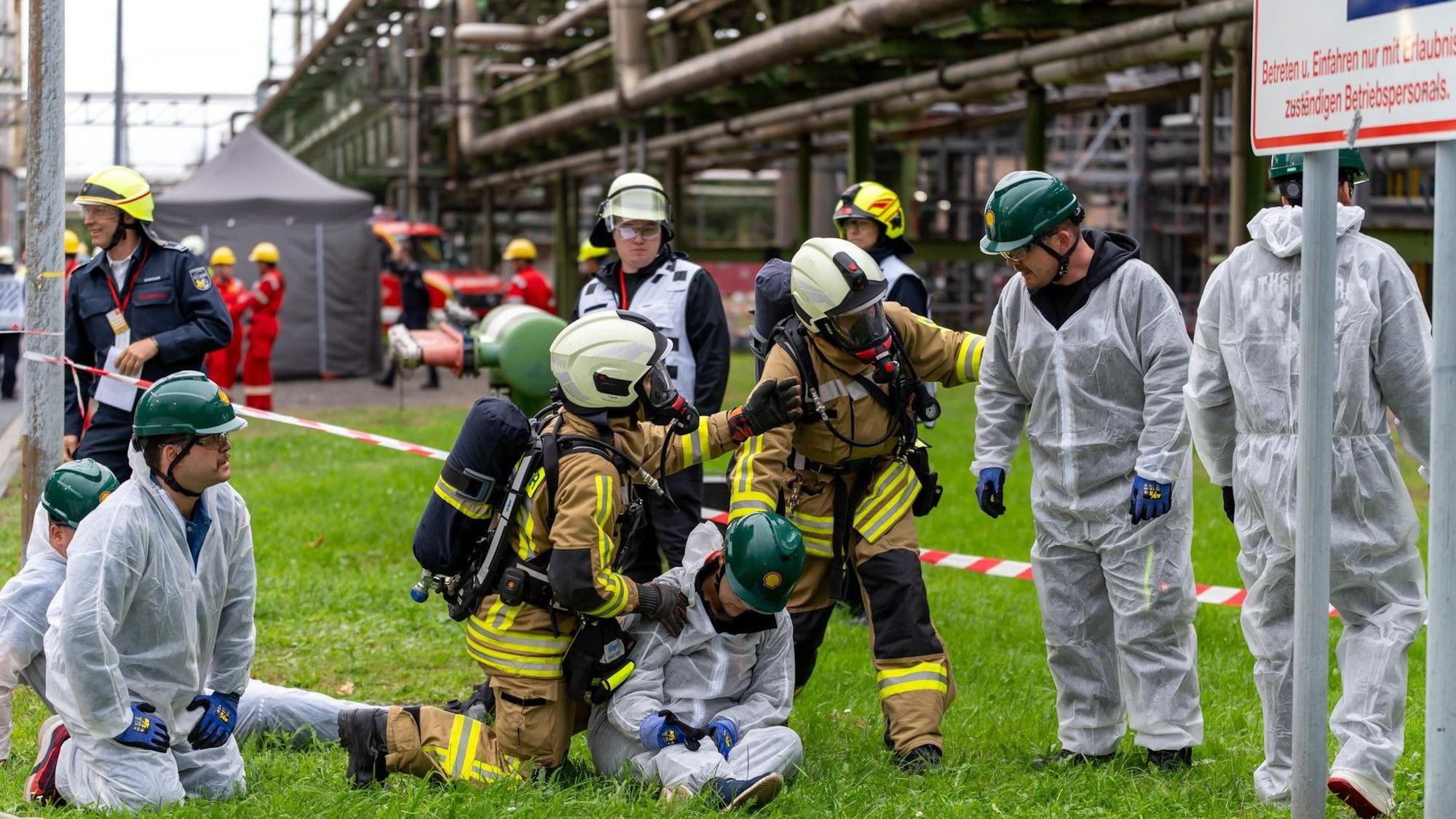 Zu sehen sind Feuerwehrleute bei einer Übung und die Darsteller von Verletzten in weißen Overalls.