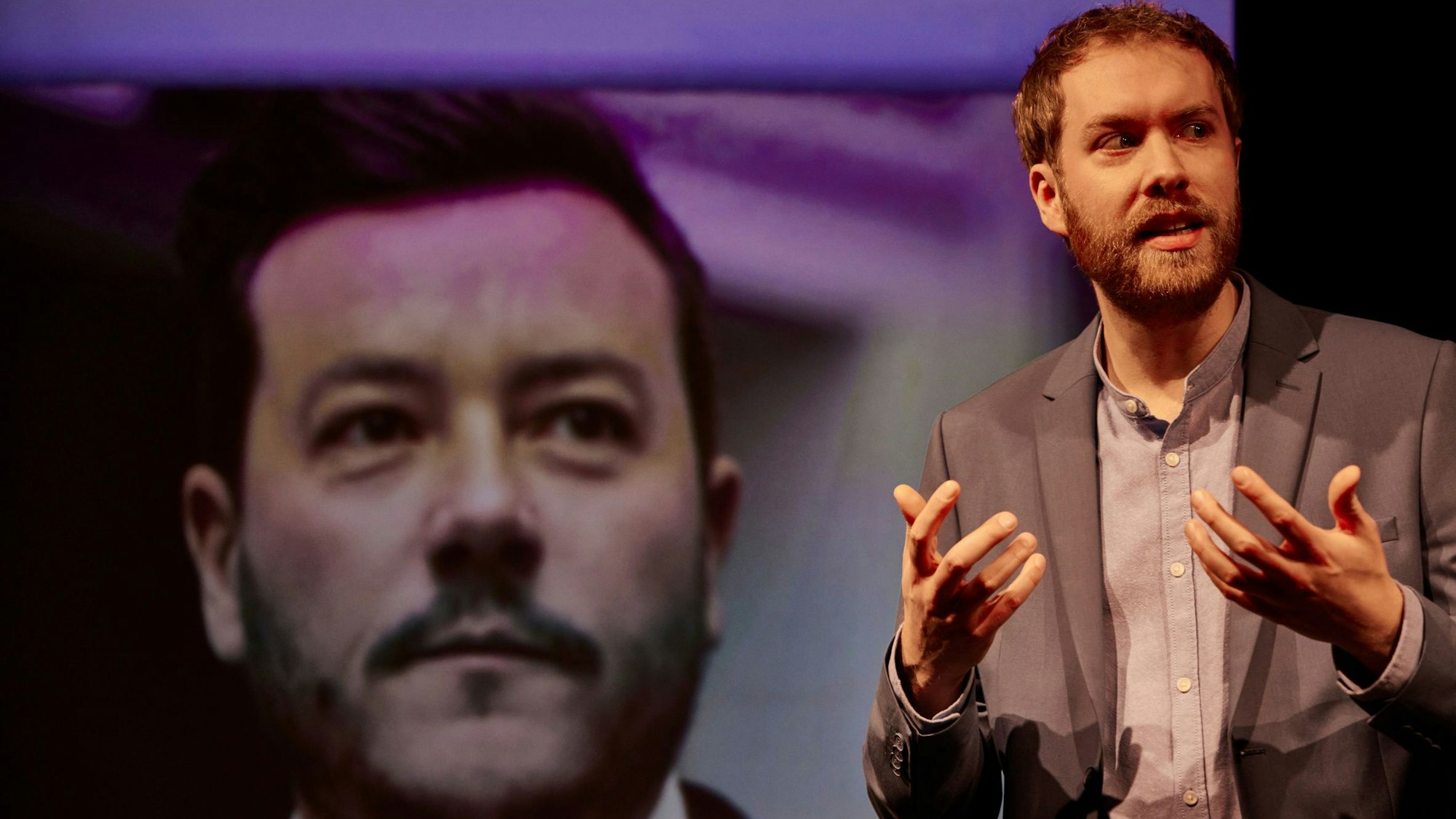 Calle Fuhr gestikuliert vor einem Bild von René Benko