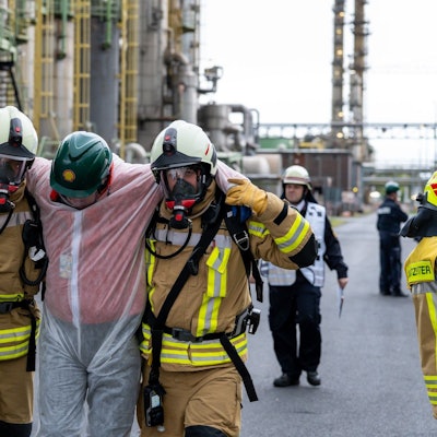 Zu sehen ist, wie zwei Feuerwehrleute bei einer Übung einen Verletzten tragen.
