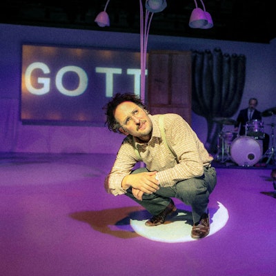 Bastian Reiber sitzt in der Hocke. Hinter ihm erscheint das Wort „Gott“