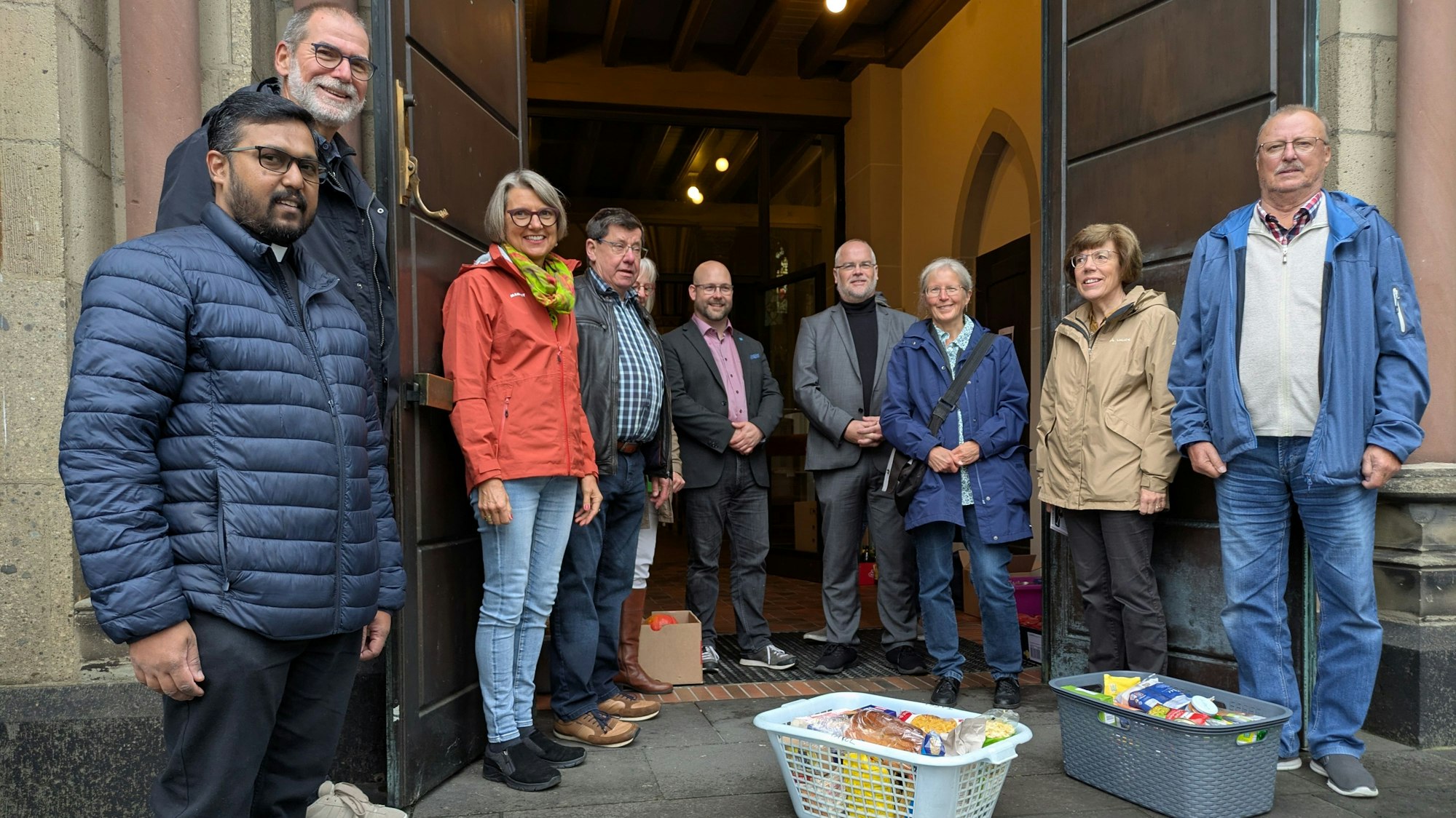 Männer und Frauen stehen mit Körben voller Lebensmittel vor einer Kirchentür.