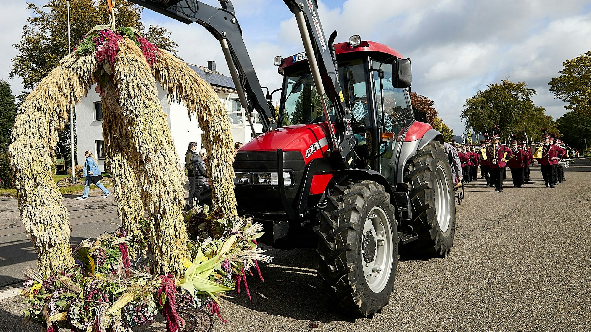 Ein Traktor hat eine Strohfigur am Frontlader hängen. Hinter dem Gefährt marschiert ein Spielmannszug.