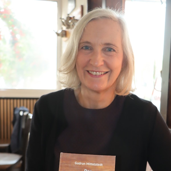 Eine blonde Frau sitzt vor einem Fenster.