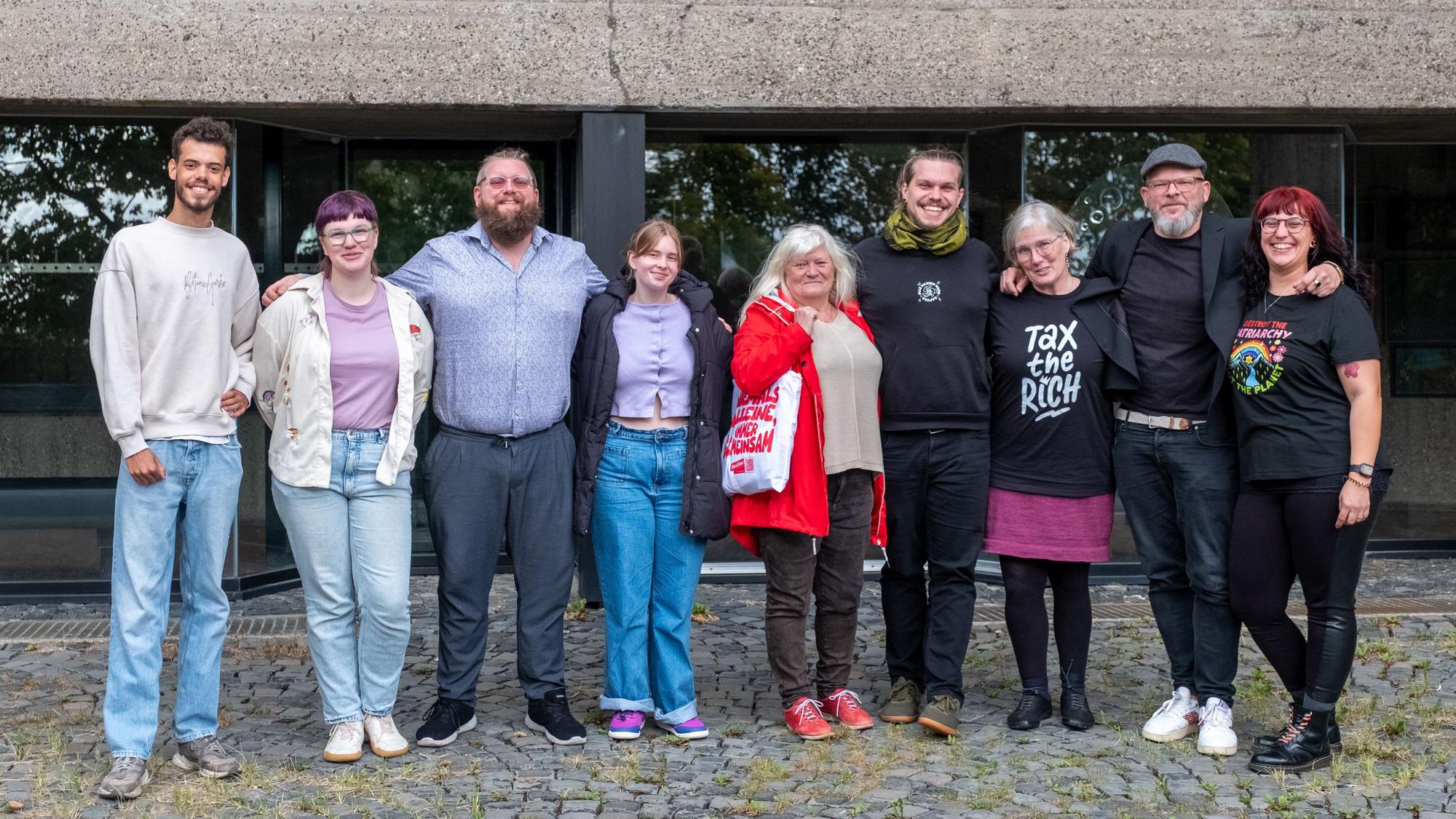 Menschen stehen vor dem Bensberger Rathaus und haken sich teilweise unter.
