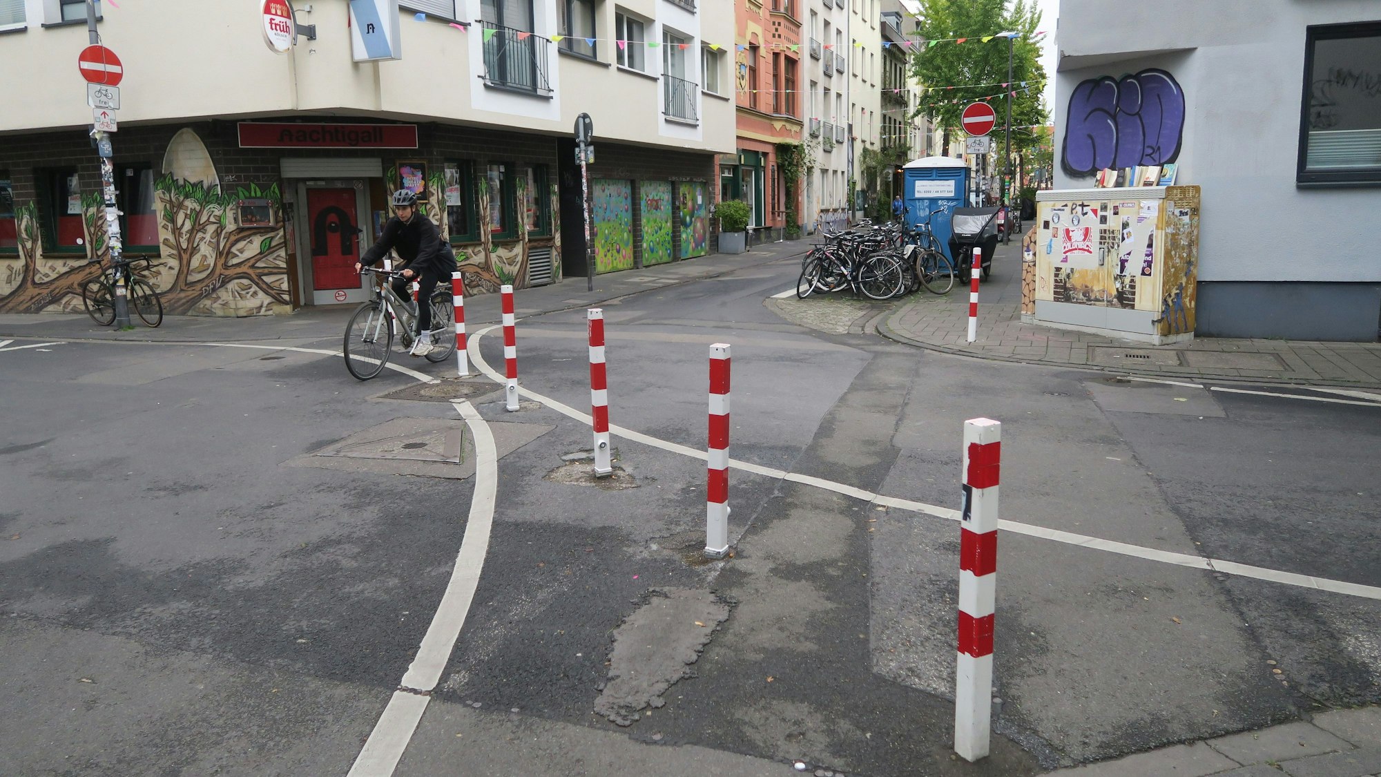 Auf einer Kreuzung zweier schmaler Straßen stehen rot-weiße-Poller.