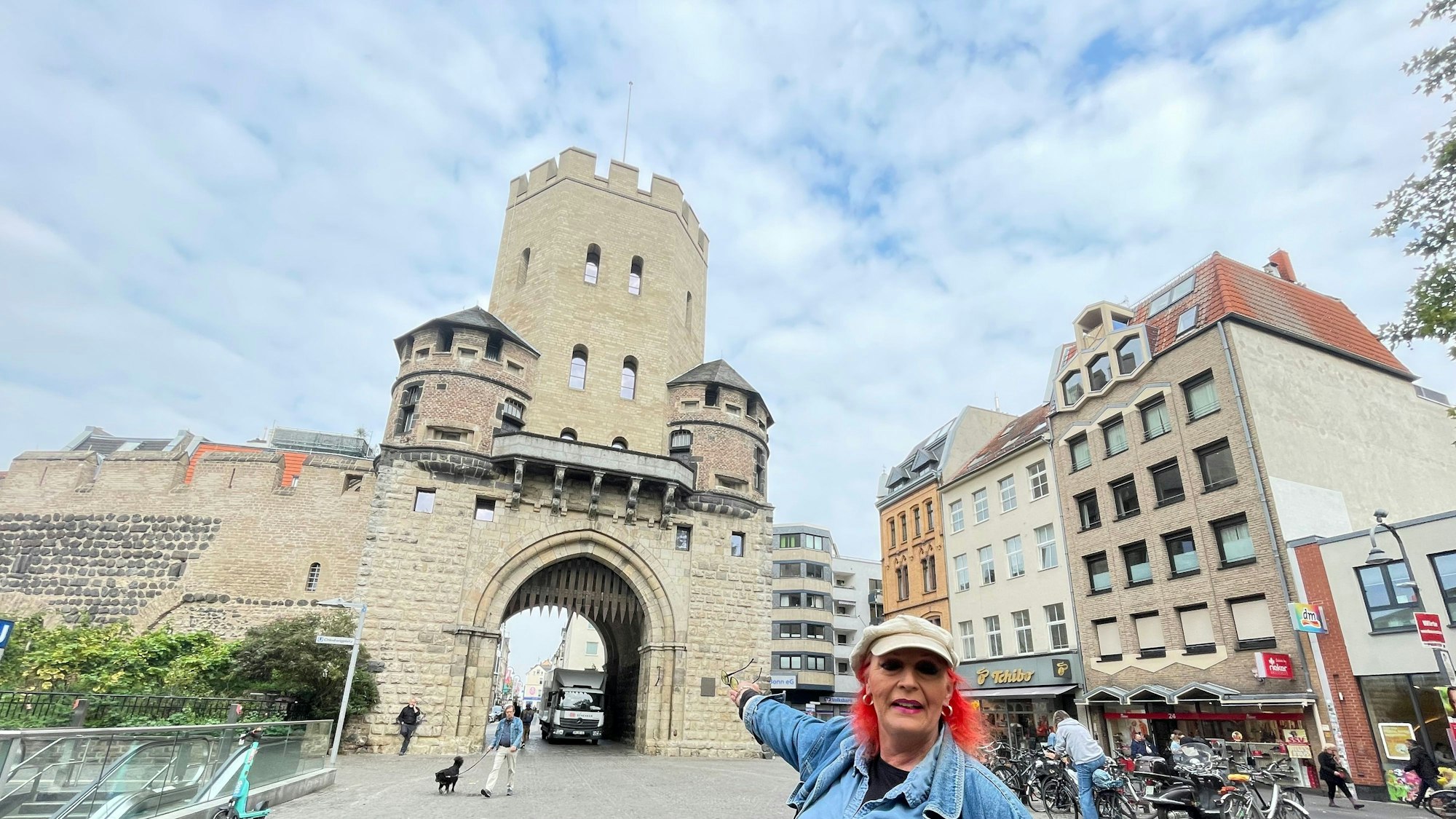 Eine Frau mit roten Haaren und Kappe, die Travestie-Künstlerin Swanee Feels, steht vor der Severinstorburg.