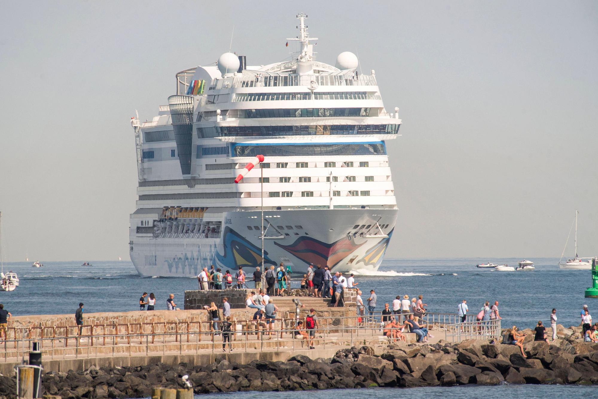 AIDA-Kreuzfahrtschiff fährt vorbei, Menschen beobachten es vom steinigen Pier am Meer