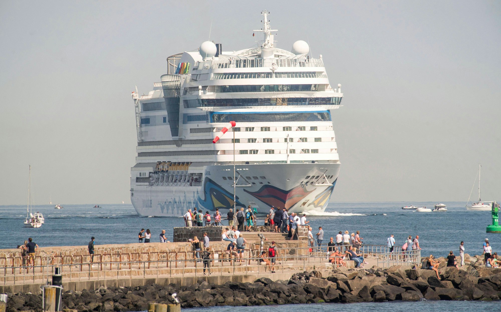 AIDA-Kreuzfahrtschiff fährt vorbei, Menschen beobachten es vom steinigen Pier am Meer