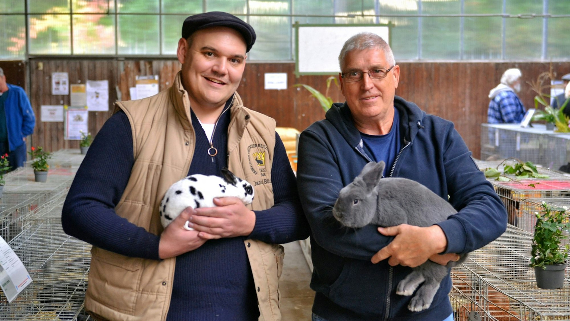 Zwei Männer stehen nebeneinander, jeder hat ein Kaninchen auf dem Arm.