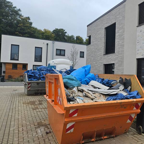 Zu sehen sind mit Sperrmüll gefüllte Container in einer Neubausiedlung.