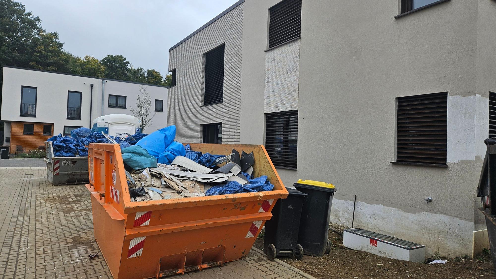 Zu sehen sind mit Sperrmüll gefüllte Container in einer Neubausiedlung.