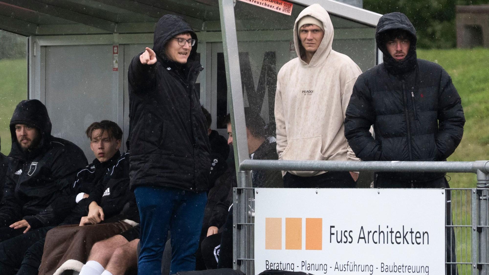 Flamersheim/Kirchheims Trainer Marco Markwald trägt eine Kapuze, spricht mit zwei Zuschauern und zeigt mit dem Finger in Richtung der Kamera.