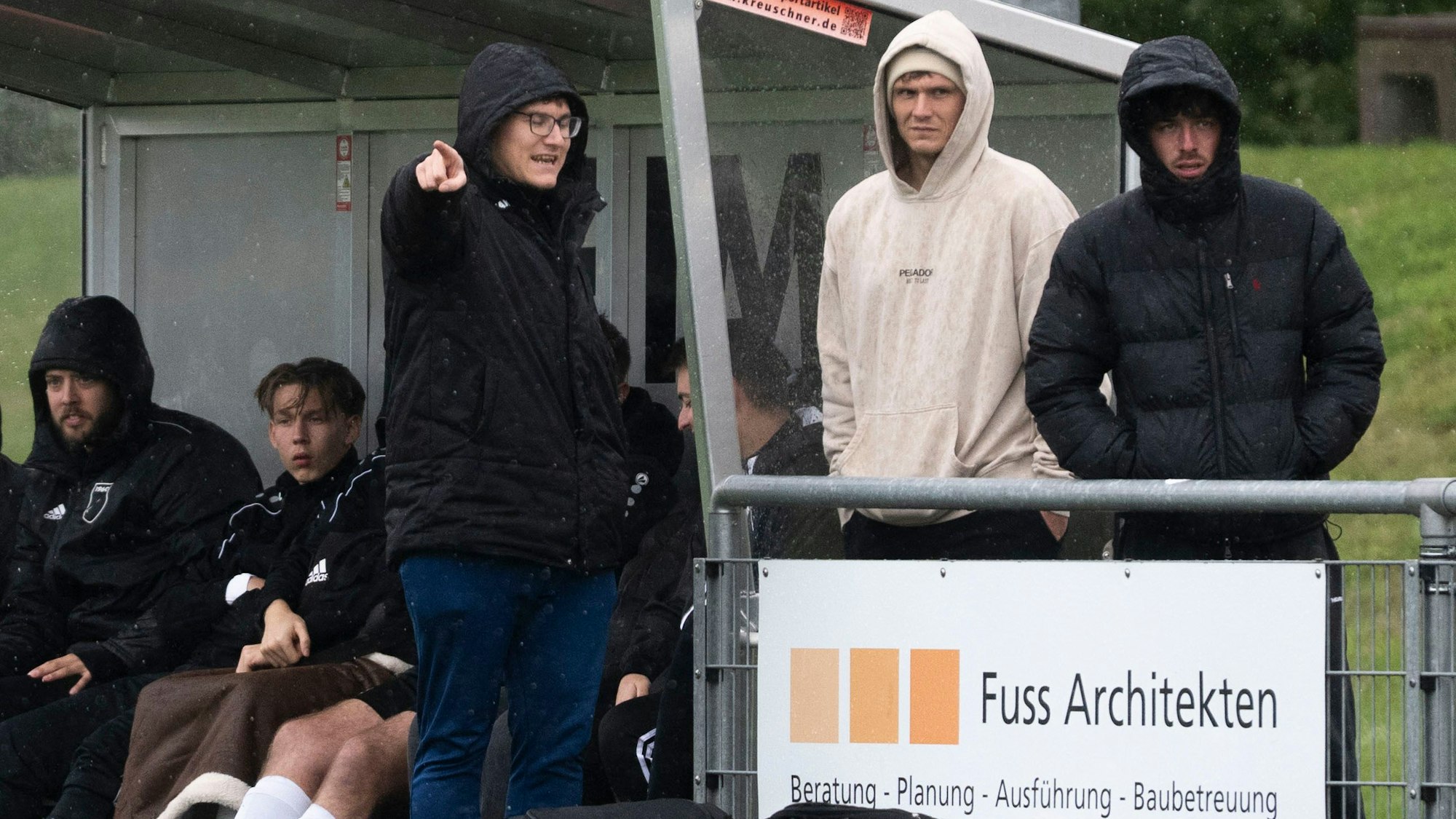 Flamersheim/Kirchheims Trainer Marco Markwald trägt eine Kapuze, spricht mit zwei Zuschauern und zeigt mit dem Finger in Richtung der Kamera.