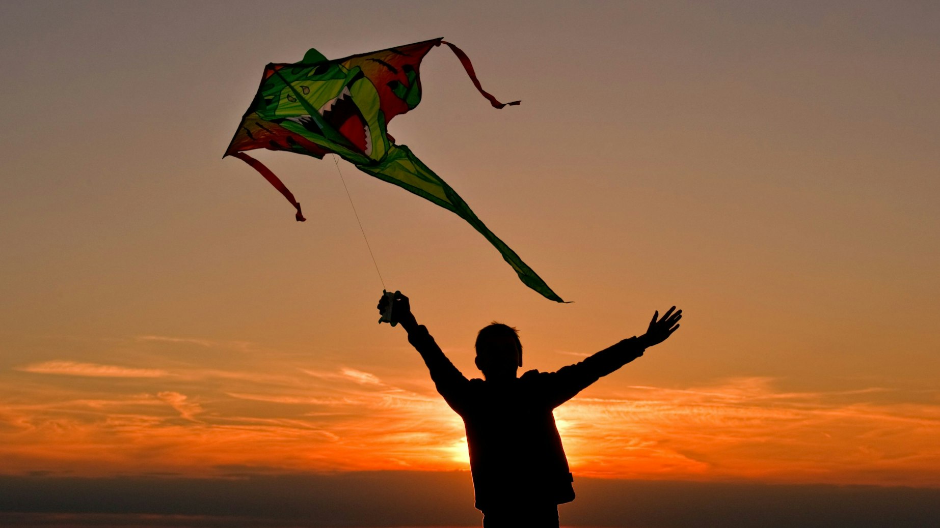 Ein Junge rennt mit seinem Drachen im Sonnenuntergang über ein Feld. (Symbolbild)