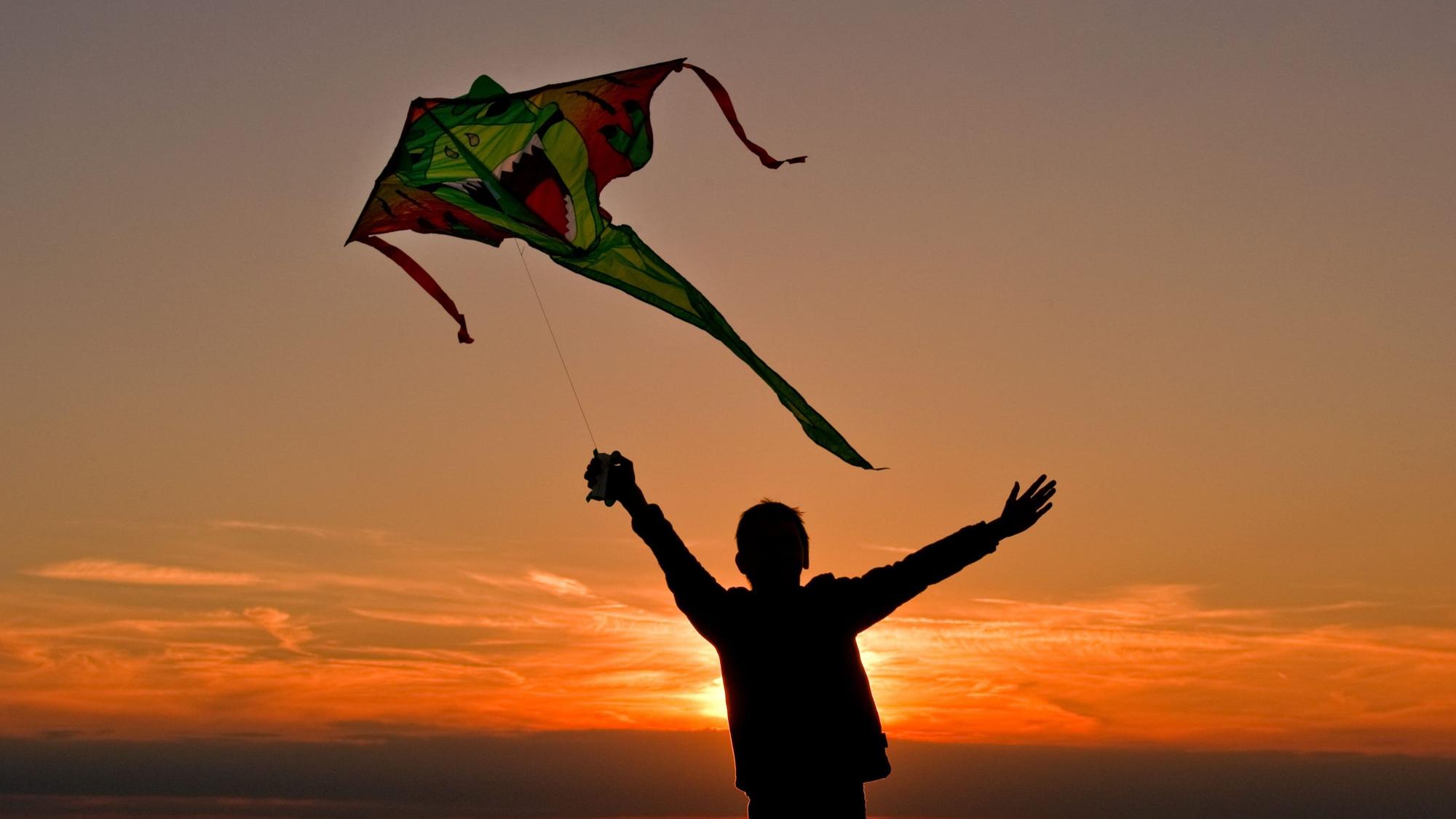 Ein Junge rennt mit seinem Drachen im Sonnenuntergang über ein Feld. (Symbolbild)